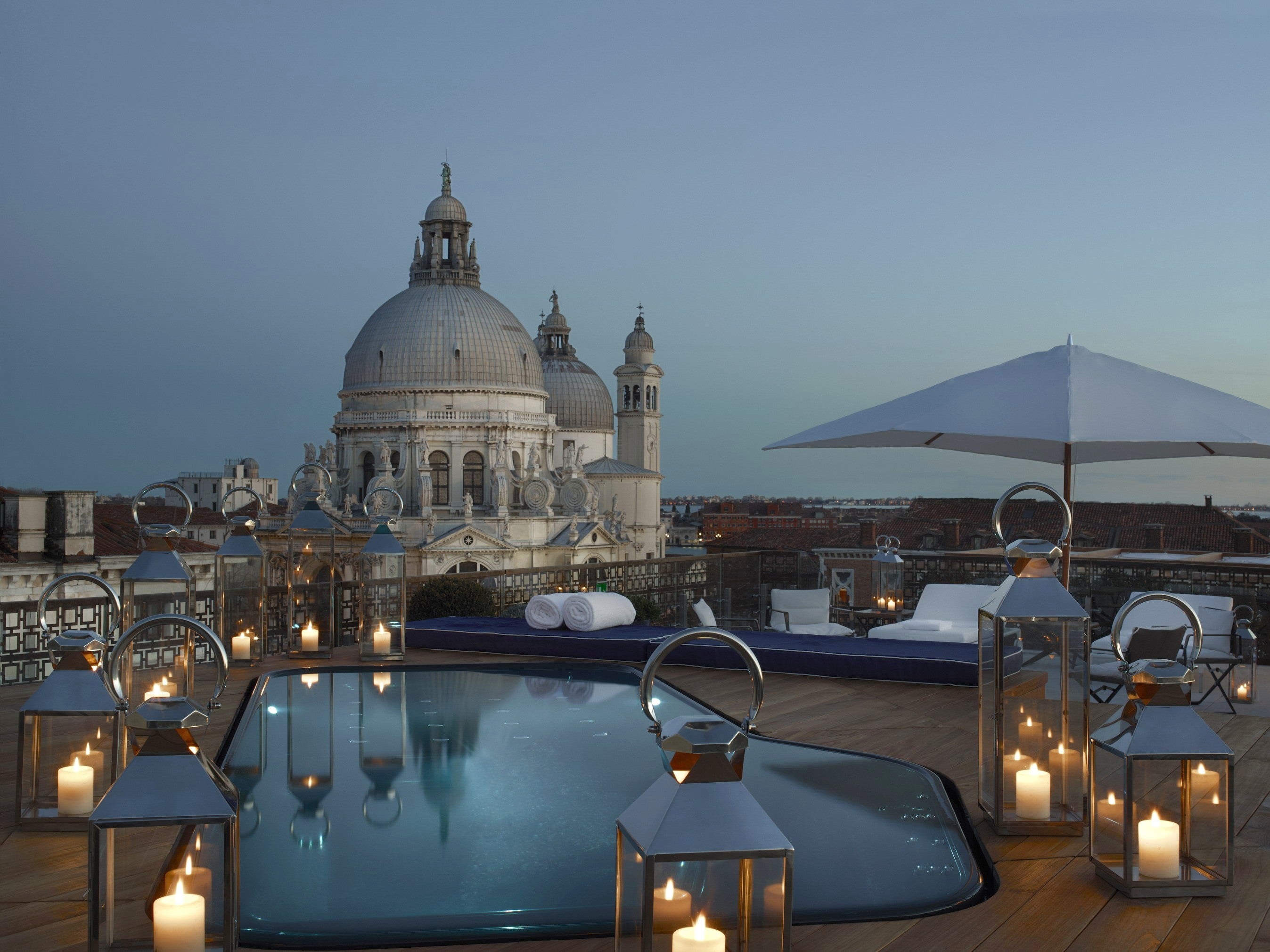 Venetian rooftop terrace with candle lanterns, lounge seating and a view of a domed church at dusk